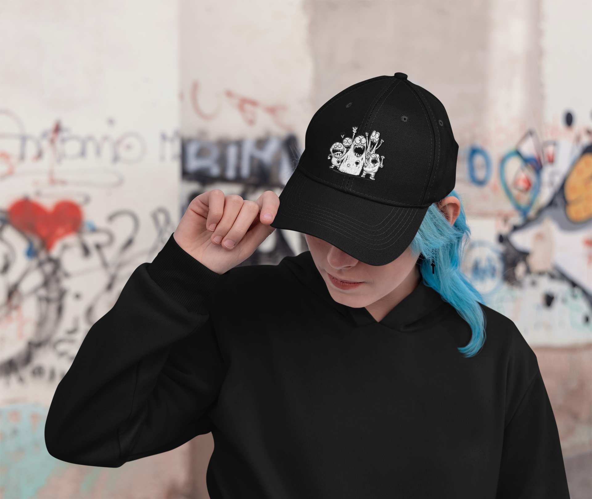 Person wearing a black cap with a design, standing against a graffiti-covered wall.